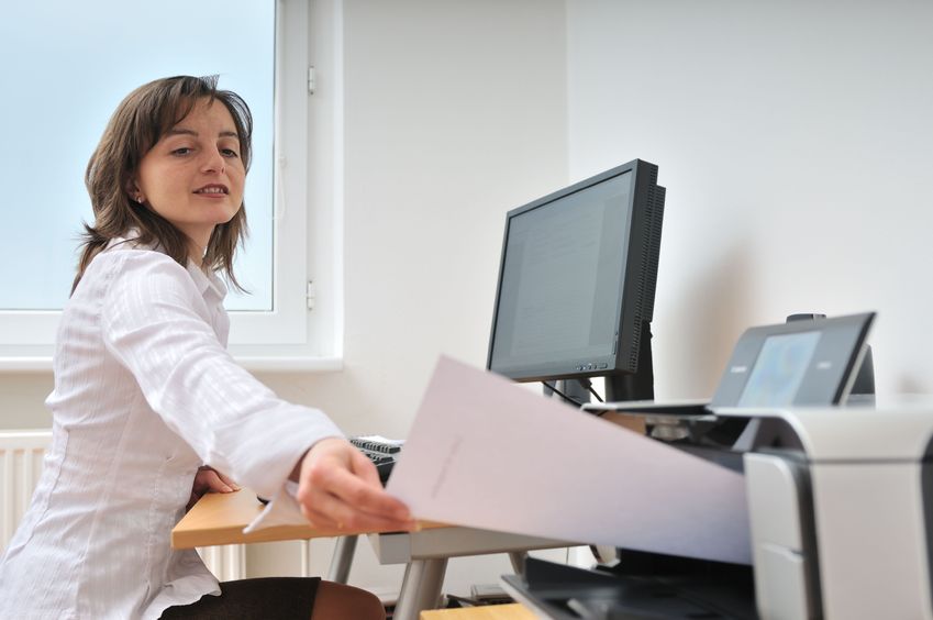 A woman at her office desk utilizing a printer.