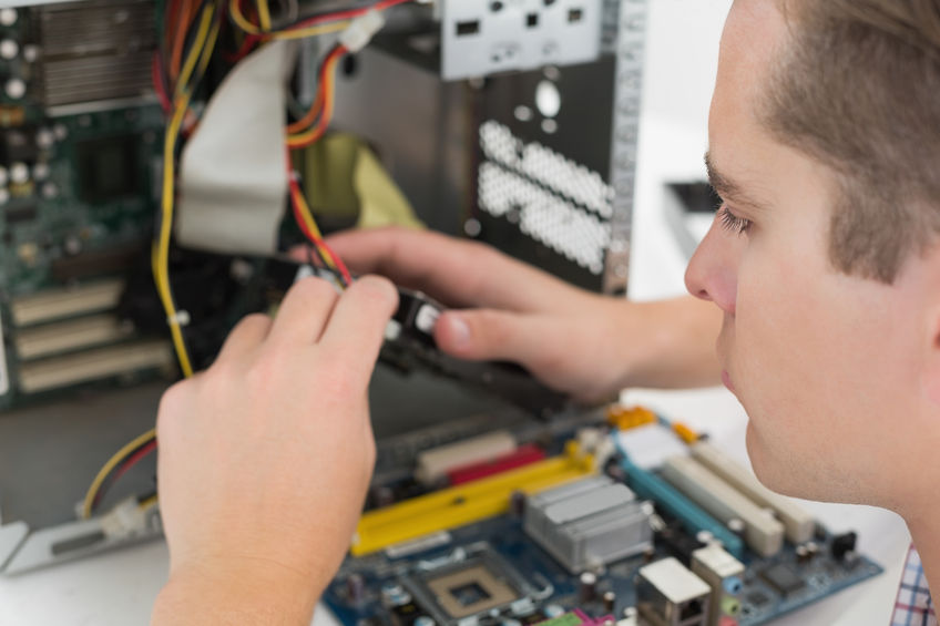 A technician working on the inside of a computer. The side has been stripped off and the motherboard place on a work unit.